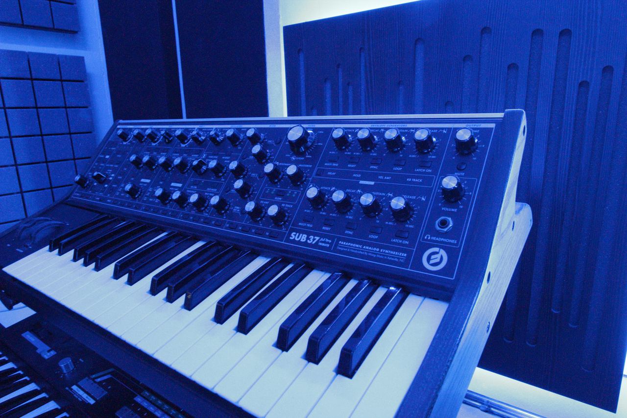 A Moog synthesizer lit in blue inside an acoustically treated Audioqube room